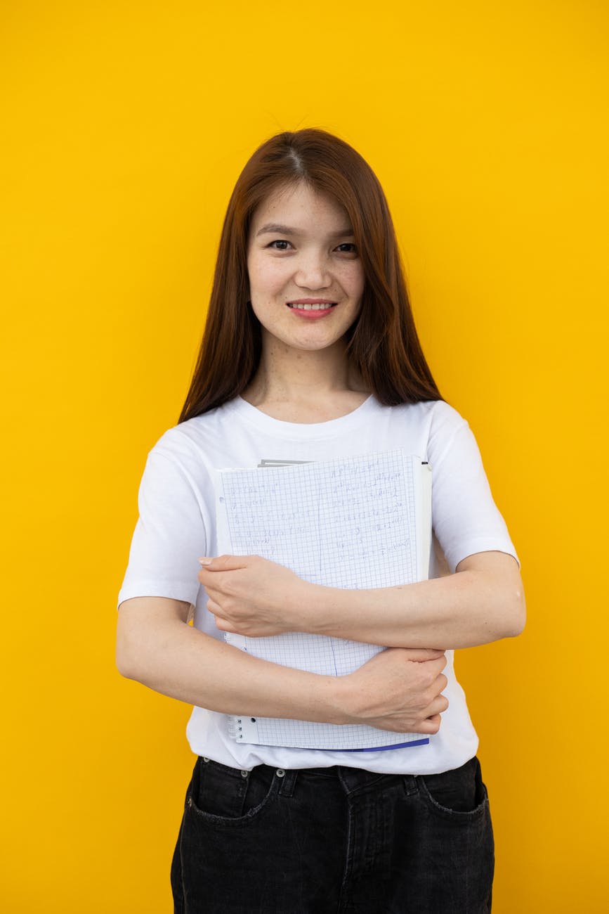 smiling young woman with documents standing against yellow background waiting for ESL English classes near me in Oklahoma City