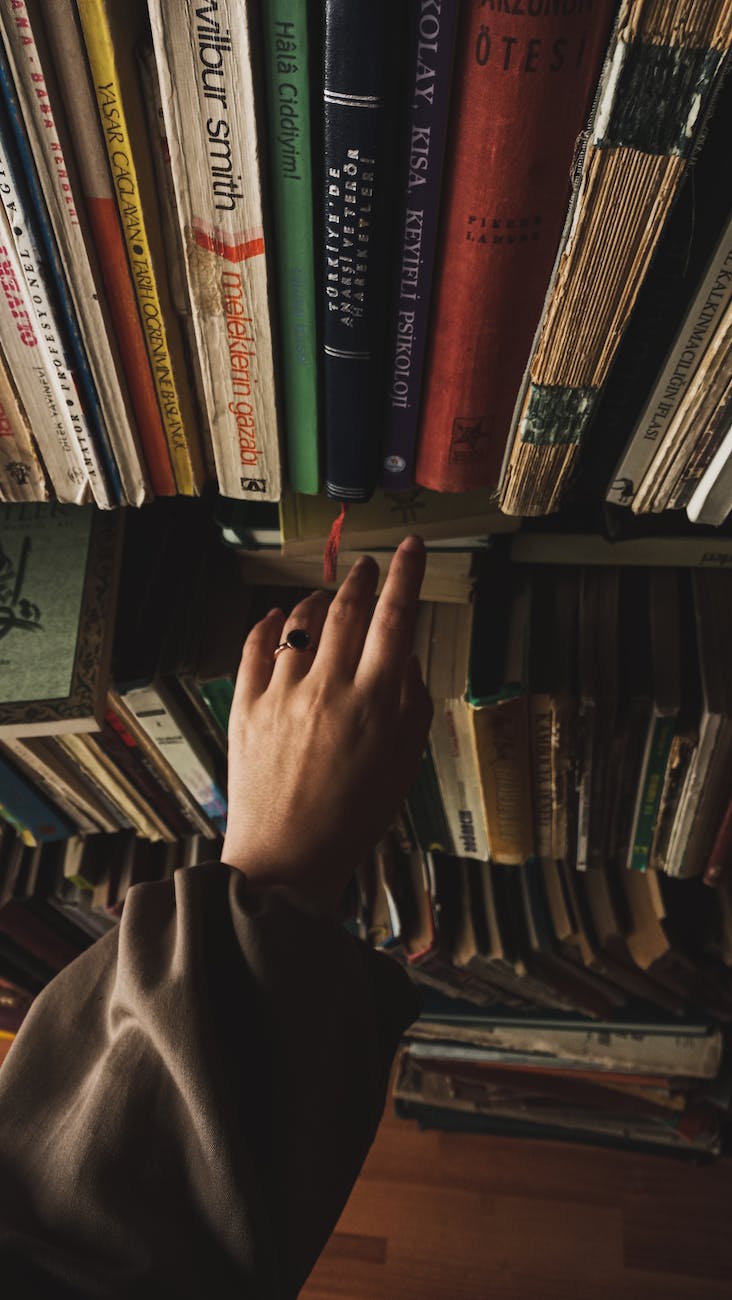 Unlock the Secret: How to Read Free English Books hand of a woman reaching for a book from a shelf at a library where you can read books for free or listen to books for free